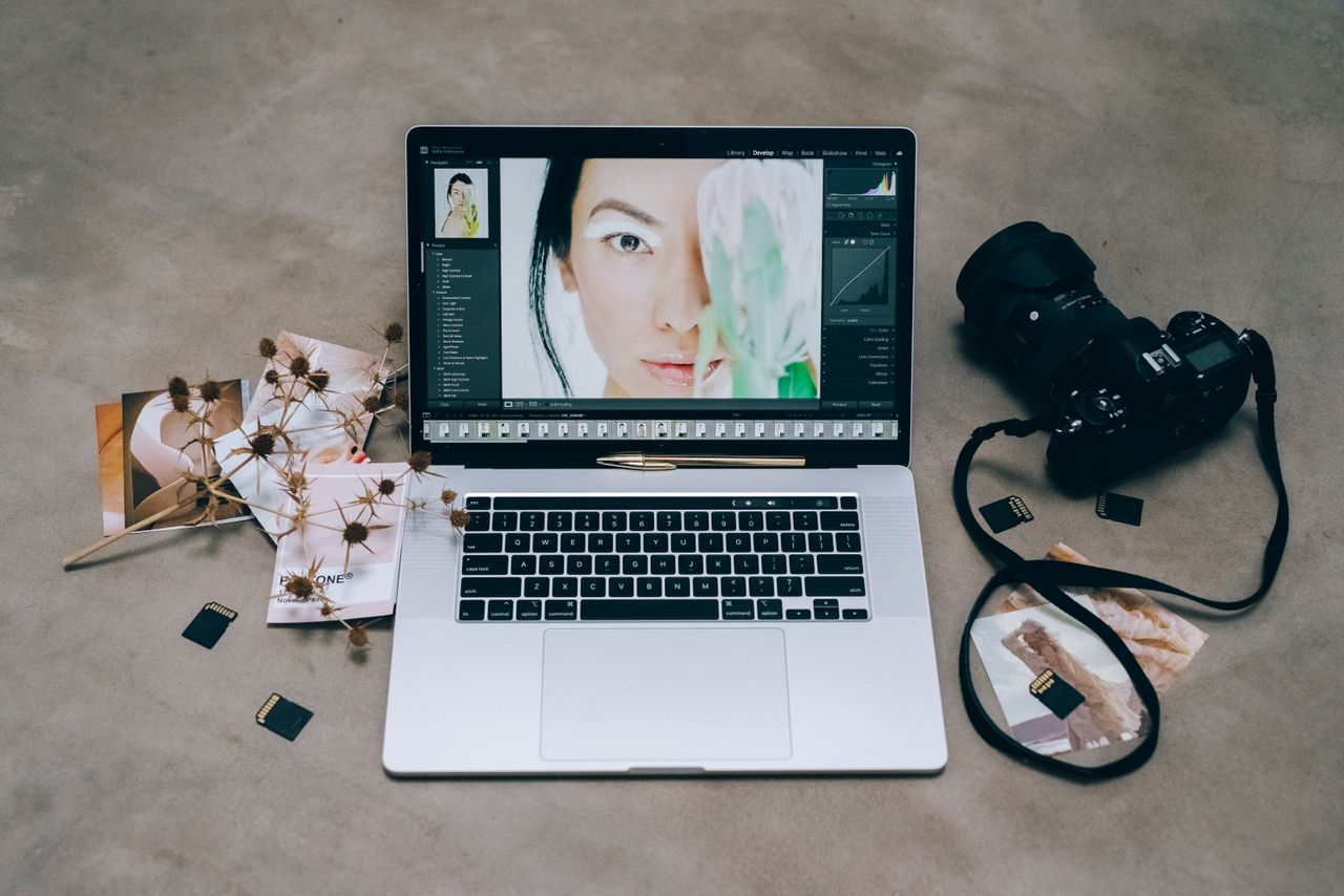 A chic photography arrangement showing a laptop editing a portrait, a camera, and several SD cards spread across a concrete surface.